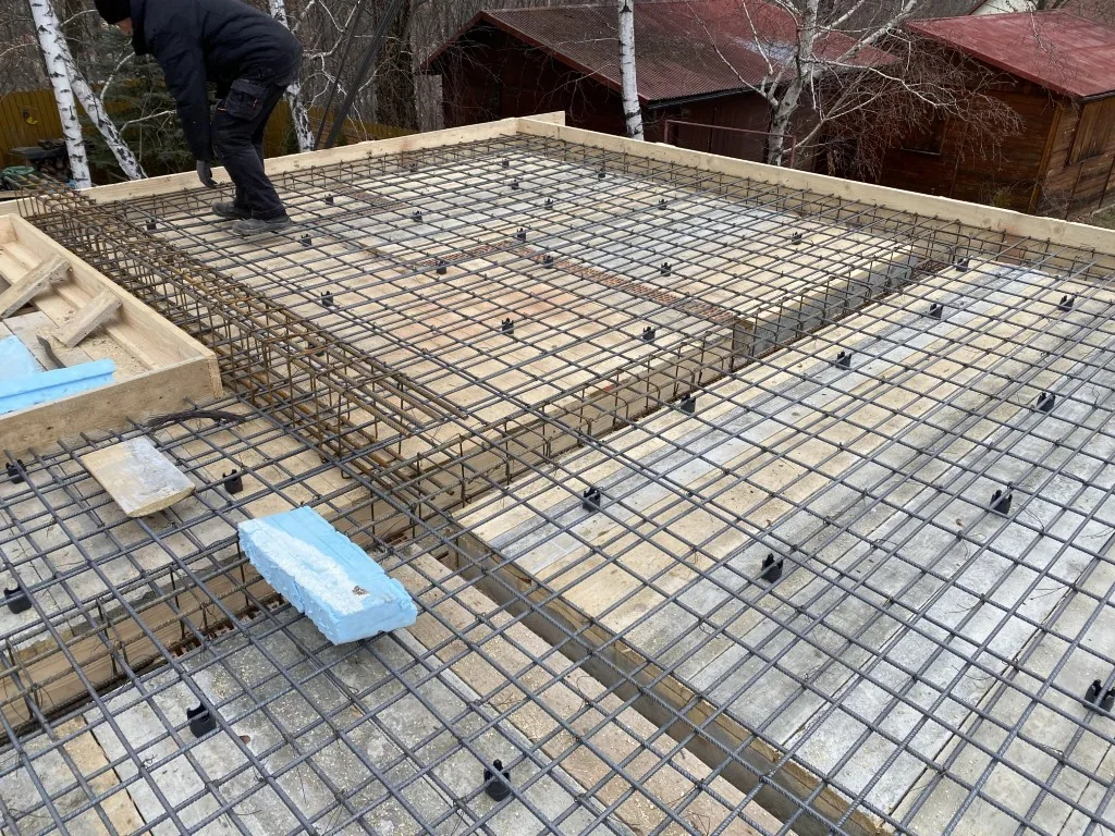 Pracownik układa gęstą dwuwarstwową siatkę zbrojeniową płyty fundamentowej